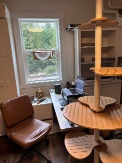A leather swivel desk chair beside a white desk with a laptop on it next to an ajar window.