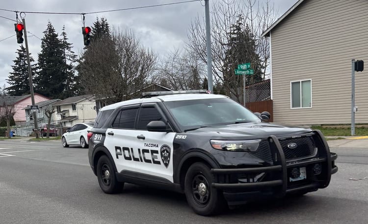 A white and black police cruiser drives through a red light at the intersection of 96th & Ainsworth in Tacoma, Washington.